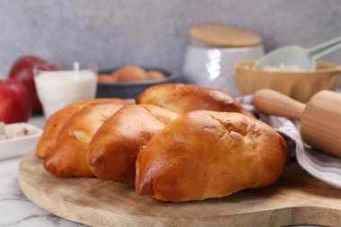 Lezzetli pirozhki (hamur tatlısı) ve beyaz mermer masa üzerindeki malzemeler, yakın plan.