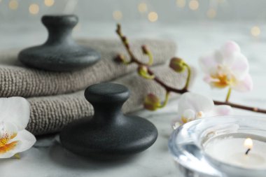 Spa taşları, orkide çiçekleri, havlular ve yanan mumlar beyaz mermer masada, yakın plan.