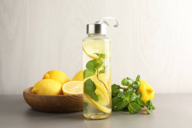 Şişe içinde naneli limon suyu, açık gri masada taze meyve ve yapraklar.