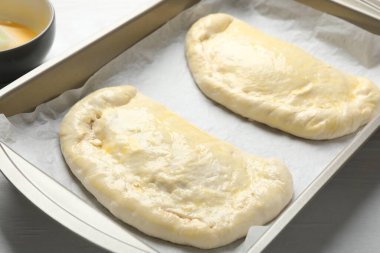 Beyaz ahşap masada pişmemiş calzone pizza, yakın plan.