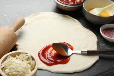 Calzone pizzası yapıyorum. Gri masada soslu ve malzemeli hamur, yakın plan.