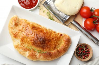 Lezzetli taze calzone pizza ve beyaz ahşap masa üzerinde malzemeler, düz yatıyordu.