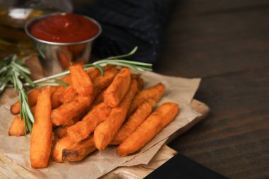 Tatlı patates kızartması, biberiye ve ketçap ahşap masada, yakın plan.