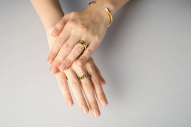 Güzel bijouterie. Açık gri arka planda şık yüzükler ve bilezik takan kadın, yakın plan.