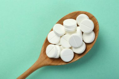 Turkuaz arka planda kaşıkta antibiyotik haplar.