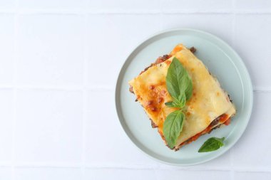 Lezzetli pişmiş lazanya, fesleğenli, beyaz fayanslı masa, üst manzara. Metin için boşluk