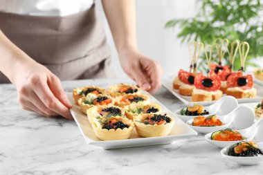 Woman with many different tasty canapes at white marble table, closeup clipart