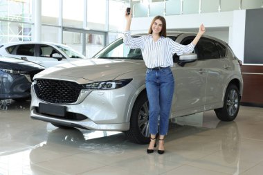 Yeni gümüş arabanın yanında anahtarı olan mutlu genç bir kadın.