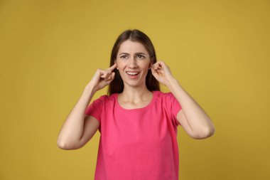 Woman covering her ears with fingers on dark yellow background clipart