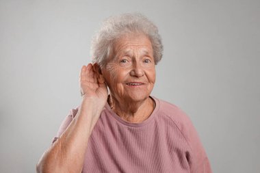 Kıdemli kadın, gri arka planda el ele hareketler gösteriyor.