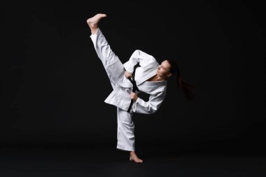 Kimonolu genç bir kadın siyah arka planda karate yapıyor.