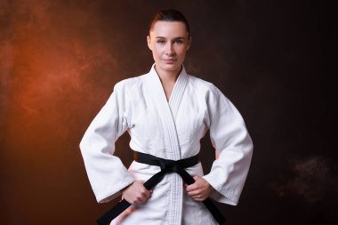 Kimonolu genç bir kadın karanlık arka planda karate yapıyor.