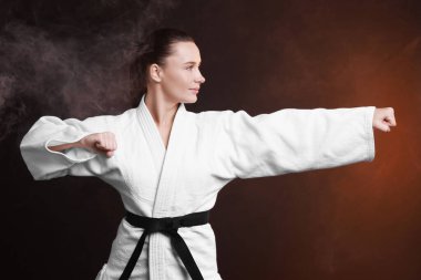 Young woman in kimono practicing karate on dark background clipart