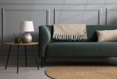 Rahat bir kanepe ve gri duvarın yanındaki yan masa.