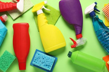 Şişelerdeki farklı temizlik ürünleri ve yeşil arka plandaki araçlar, düz konum