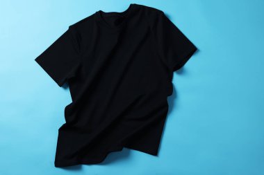 Açık mavi arkaplanda bir siyah tişört, üst görünümde.