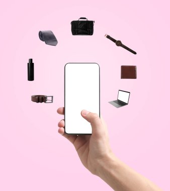 Pembe arka planda online alışveriş için cep telefonu kullanan adam, yakın plan. Farklı mallar etrafta uçuşuyor. Boş ekranlı aygıt