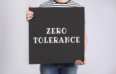 Man holding poster with words Zero Tolerance on light grey background, closeup clipart