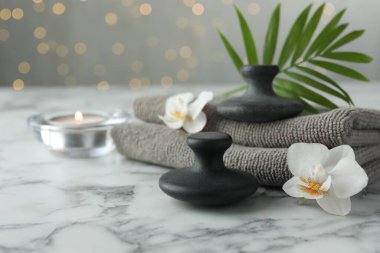 Spa taşları, orkide çiçekleri, havlular, yanan mum ve yaprak beyaz mermer masa, yakın çekim