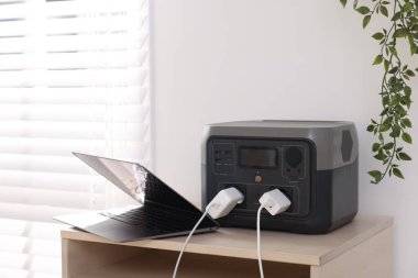İçerideki ahşap masada taşınabilir elektrik santralinden dizüstü bilgisayar şarj ediliyor.