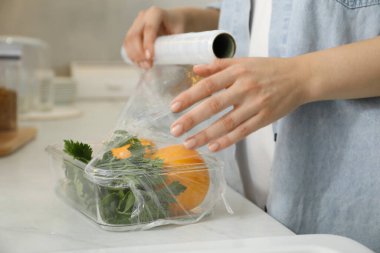 Mutfaktaki tezgahta plastik gıda ambalajını sebzelerle dolduran kadın, yakın plan.