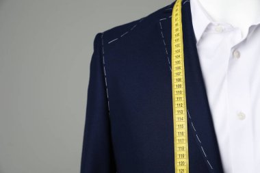 Yarı-hazır ceket, terzi ölçüm bandı ve gri arka planda beyaz gömlek, yakın plan.