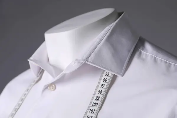 Male mannequin with white shirt and measuring tape on grey background, closeup