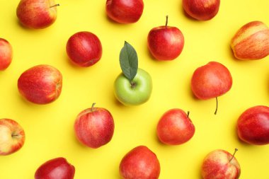 Flat lay composition with green apple surrounded by red ones on yellow background clipart