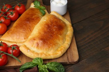 Lezzetli vejetaryen calzones fesleğen, mozzarella peyniri ve domatesler ahşap masada, yakın plan. Metin için boşluk