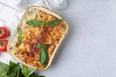Pişirme kabında nefis pişmiş lazanya, açık gri masada fesleğen ve domates, üst manzara. Metin için boşluk