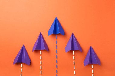 Mor ve turuncu arka planda uçuş yolları olan mavi kağıt uçaklar. Yörünge için kesilmiş çizgiler