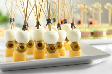 Farklı peynir ve yeşil zeytinli kanepeler beyaz masada, yakın plan.