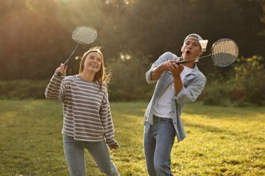 Genç kadın ve adam güneşli bir günde parkta badminton oynuyorlar.