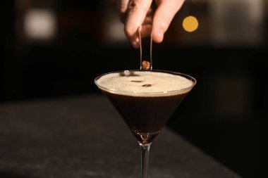 Barmen bardağa kahve çekirdeği koyuyor koyu masada nefis espresso martini ile, yakın plan.