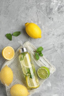 Şişe içinde nane aromalı limon suyu, taze yapraklar ve gri masada meyveler.