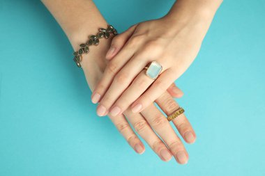 Güzel bijouterie. Farklı tarz yüzükler takan ve açık mavi arka planda bilezik takan bir kadın.