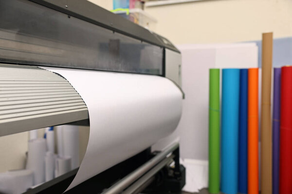 Wide-format printer with paper indoors, closeup. Printing house