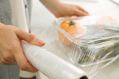Mutfaktaki tezgahta plastik gıda ambalajını sebzelerle dolduran kadın, yakın plan.