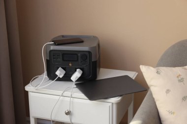 İçerideki komodinin üzerinde taşınabilir elektrik santralinden şarj olan aygıtlar