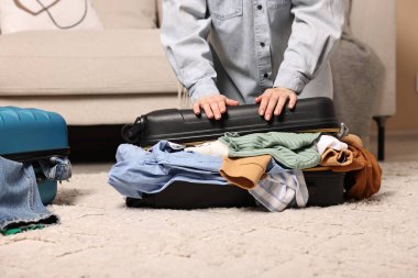 Farklı kıyafetlerle dolu bavulu kapatmaya çalışan bir kadın.