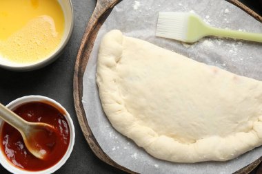 Pişmemiş calzone pizza, sos ve yumurta sarısı gri masada, düz yerde.