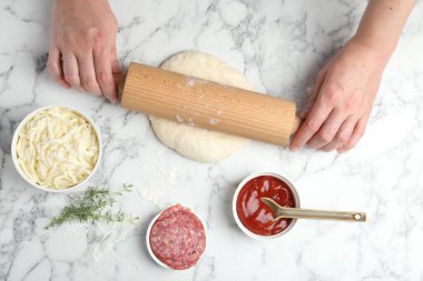 Calzone pizzası yapıyorum. Beyaz mermer masada merdaneyle hamuru şekillendiren kadın.