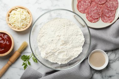 Calzone pizzası yapıyorum. Beyaz mermer sehpada farklı malzemeler var.
