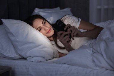 Kötü alışkanlık. Genç bir kadın gece yatakta akıllı telefon kullanıyor.