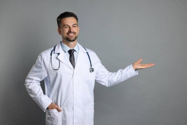 Steteskoplu gülümseyen doktor gri arka planda bir şeye bakıyor.