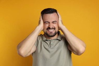 Man covering his ears on orange background clipart