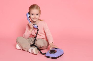 Pembe arka planda telefonu olan şirin küçük bir kız. Mesaj için yer var.