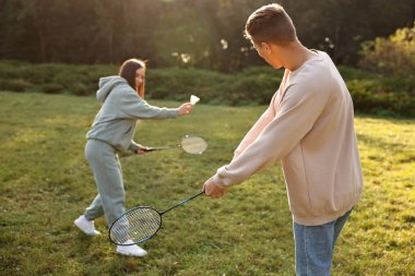 Güneşli bir günde parkta badminton oynayan genç bir kadın ve erkek.