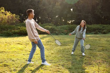Güneşli bir günde parkta badminton oynayan genç bir kadın ve erkek.