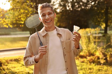 Güneşli bir günde parkta badminton raketi ve pipisi olan mutlu genç bir adam.